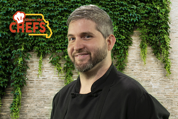 Chef Jody Easter smiles slyly in front of a brick wall covered in ivy